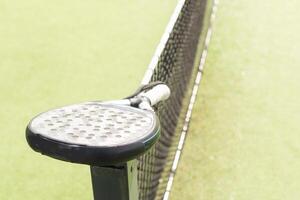 Padel racket and padel ball on a green court in the sunset photo