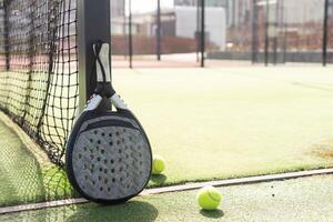 padel raqueta y padel pelota en un verde Corte en el puesta de sol foto