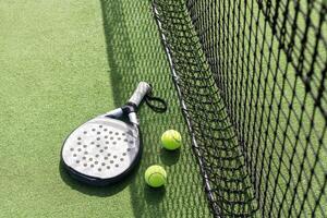 Padel racket and padel ball on a green court in the sunset photo