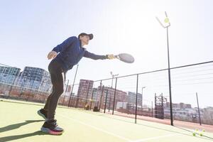 A girl in sportswear is training on a paddle tennis court. The girl is hitting the ball against the glass to make a rebound. Concept of women playing paddle. photo