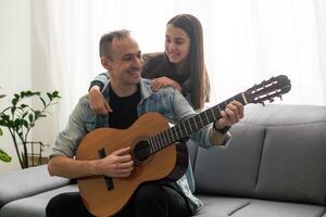 Father guy teaching girl teenager daughter guitar playing at home. Family musical lessons with strings instrument photo