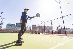 A girl in sportswear is training on a paddle tennis court. The girl is hitting the ball against the glass to make a rebound. Concept of women playing paddle. photo