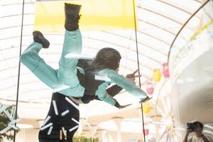 Excited teenage girl in helmet flying in aerodynamic tube wind tunnel. Skydiving training. photo