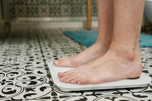 Woman checking her weight on weighing scales in bathroom photo