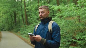 gut aussehend jung kaukasisch Mann mit Handy, Mobiltelefon Telefon zu finden seine Ort im das Berg Wald. Straße Reise, Transport, reisen, Technologie und Menschen Konzept. video