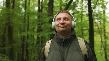 joven alegre activo chico deportivo caminando con auriculares móvil teléfono disfrutando escuchando a música al aire libre a bosque video