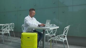 viaggiare, il computer portatile e grave caucasico uomo seduta Lavorando su il computer portatile mentre in attesa atterraggio nel aeroporto. invio Presto testo prima decollare. video