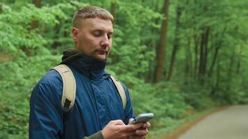 Handsome young Caucasian man using mobile phone to find his location in the mountain woods. Road trip, transport, travel, technology and people concept. video