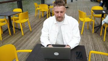 knap Kaukasisch leerling gebruik makend van laptop computer aan het kijken afstand online aan het leren congres klas, afgelegen Universiteit webinar of hebben virtueel klas vergadering in straat outdors cafe creatief ruimte. video