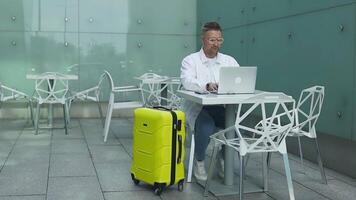 Busy businessman sitting at the airport using laptop and mobile phone next to the style cafe while waiting flight at modern airport video