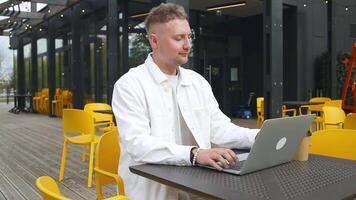 gut aussehend kaukasisch Schüler mit Laptop Computer Aufpassen Entfernung online Lernen Seminar Klasse, Fernbedienung Universität Webinar oder haben virtuell Klassenzimmer Treffen im Straße Außenseiter Cafe kreativ Raum. video