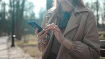 Happy pretty girl student hands user holding cell phone using education tech apps looking at smartphone texting messages standing outside. Mobile online applications concept. video