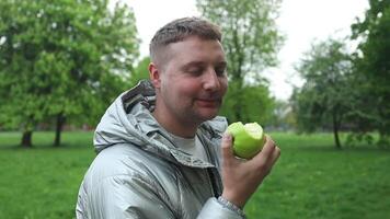 passen Mann Essen ein Apfel im das Landschaft. kaukasisch männlich beißt ein Apfel beim Frühling Stadt Park. vegan männlich und Entgiftung mit Gewicht Verlust, Gesundheitswesen und organisch Früchte. video