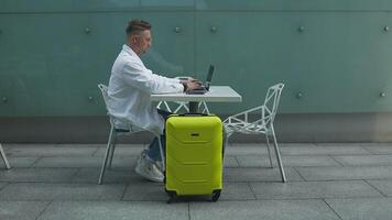 viaggiare, il computer portatile e grave caucasico uomo seduta Lavorando su il computer portatile mentre in attesa atterraggio nel aeroporto. invio Presto testo prima decollare. video