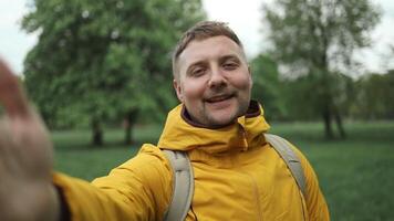 frio barbado caucásico hombre en pie en naturaleza parque utilizando móvil teléfono. retrato de sonriente joven masculino turista haciendo un selfie o llamada a verde selva bosque antecedentes. video