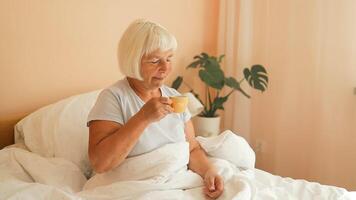 Caucasian 60s woman having morning coffee in bed. Female relaxing in bedroom having tea. video