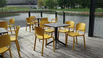 Black tables with yellow modern charis in cafe on the street. Empty cafe in the summer morning. Modern outdoor cafe. Street cafe. Modern Terrace. Empty restaurant. video