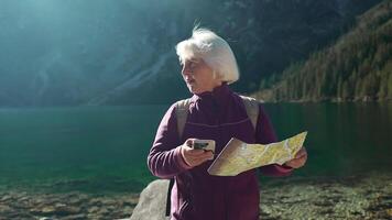 turista caminante mayor mujer mochilero con mapa mirando a lago. verano viaje en naturaleza. estilo de vida, unión, naturaleza concepto video