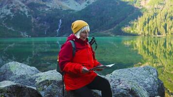 Happy senior woman tourist search a map in mountains at Morskie Oko lake near Zakopane, Tatra Mountains, Poland. Family travel concept. video