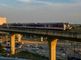 nonthaburi-tailandia abril dieciséis, 2024 el eléctrico cielo tren mrt púrpura línea pasa mediante central puerta oeste Departamento Tienda el más grande compras plaza en el noche a explosión sí, nonhaburi tailandia foto