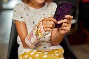 Teen girl with a broken arm orthopedic cast use smartphone photo