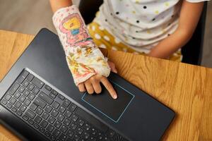Teen girl with a broken arm orthopedic cast studying online photo