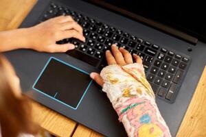 Teen girl with a broken arm orthopedic cast studying online photo