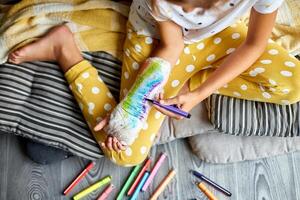 Teen girl with a broken arm at home draws an orthopedic cast photo