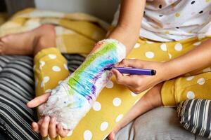 Teen girl with a broken arm at home draws an orthopedic cast photo