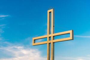 Golden cross against a background of blue sky with clouds. A minimalistic view of a gold-colored cross against the sky. photo
