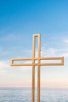 Golden cross against a background of blue sky with clouds. A minimalistic view of a gold-colored cross against the sky. photo