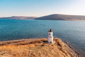 ver de el faro en el costa y el isla en el horizonte. faro en el apuntalar de un calma mar en un soleado día. russky isla, vladivostok, Rusia. foto