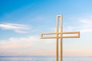 Golden cross against a background of blue sky with clouds. A minimalistic view of a gold-colored cross against the sky. photo