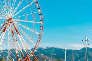 View of the Ferris wheel attraction against a background of blue sky between palm trees. Ferris wheel in the Georgian city of Batumi. photo