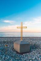 Golden cross on the sea and blue sky. A minimalistic view of a golden cross against the backdrop of a cloudy horizon. photo