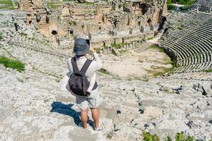 A male tourist enjoys a walk through the amphitheater among the ruins of the ancient city of Perge, in Turkey. The tourist looks around the ancient city of Perge with fascination and takes photographs photo