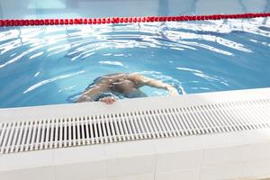 un pensionista de 70 años descansa y nada en el piscina en un limpio, azul piscina en el Fresco aire en vacaciones. foto