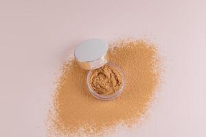 Top view of an open jar with loose powder of beige, bronze tone stands on a scattered sample of powder. A copy of the space. Make up. photo