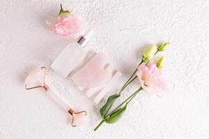 White matte bottle with natural remedy, serum, massage oil on white plaster embossed podium among flowers. Care concept. photo