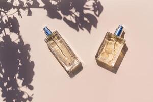 Two bottles with perfume or spray on a beige background in the rays of the sun and the shade of the leaves tree. top view. mockup. presentation photo