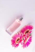 Elegant bottle of women's perfume with delicate fragrances on a white satin background with flowers pink gerberas. Empty packaging. presentation. photo