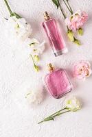 dos diferente botellas de De las mujeres perfume con un floral fragancia en un blanco texturizado antecedentes entre flores parte superior vista. plano poner. perfume concepto. foto