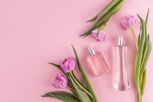 Two stylish glass bottles with perfume on a pink background among spring flowers. A copy space. Top view. Perfume and beauty concept. photo