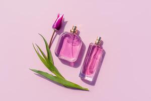 Two different bottles of perfume or eau de toilette on a lilac background with a tulip. Top view. Beauty concept. Presentation of the fragrance. photo