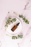 Cosmetic bottle with natural face and body care product with eucalyptus oil extract on a white round tray. Marble vertical background. photo