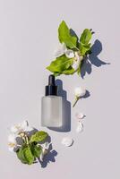 A matte bottle of a cosmetic product for daily face and body skin care on a light background among the twigs of a blossoming apple tree. vertical. photo