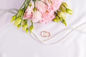 dos oro clásico Boda anillos en un blanco satín antecedentes con Fresco rosado autómata flores un Copiar espacio. tarjeta postal. invitación. cubrir foto