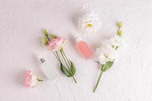 dos mate cosmético botellas con un cuentagotas con un natural piel cuidado producto para cara en un blanco antecedentes entre delicado primavera flores plano laico foto