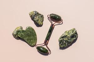 Natural Stone Roller Massager, Gua Sha Jade Scraper On Beige Background Among Natural Green Stones. top view. photo