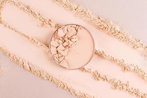 A classic compact powder with broken pieces of texture in a round block on a beige swatch background. Top view. A copy space. Product advertising. photo